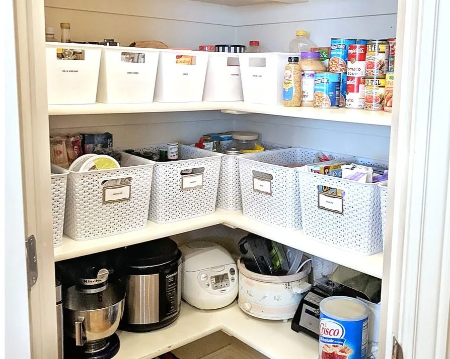 After: the same corner pantry organized, with labeled white bins on the same shelves and the rice cooker and slow cooker in a tidy row